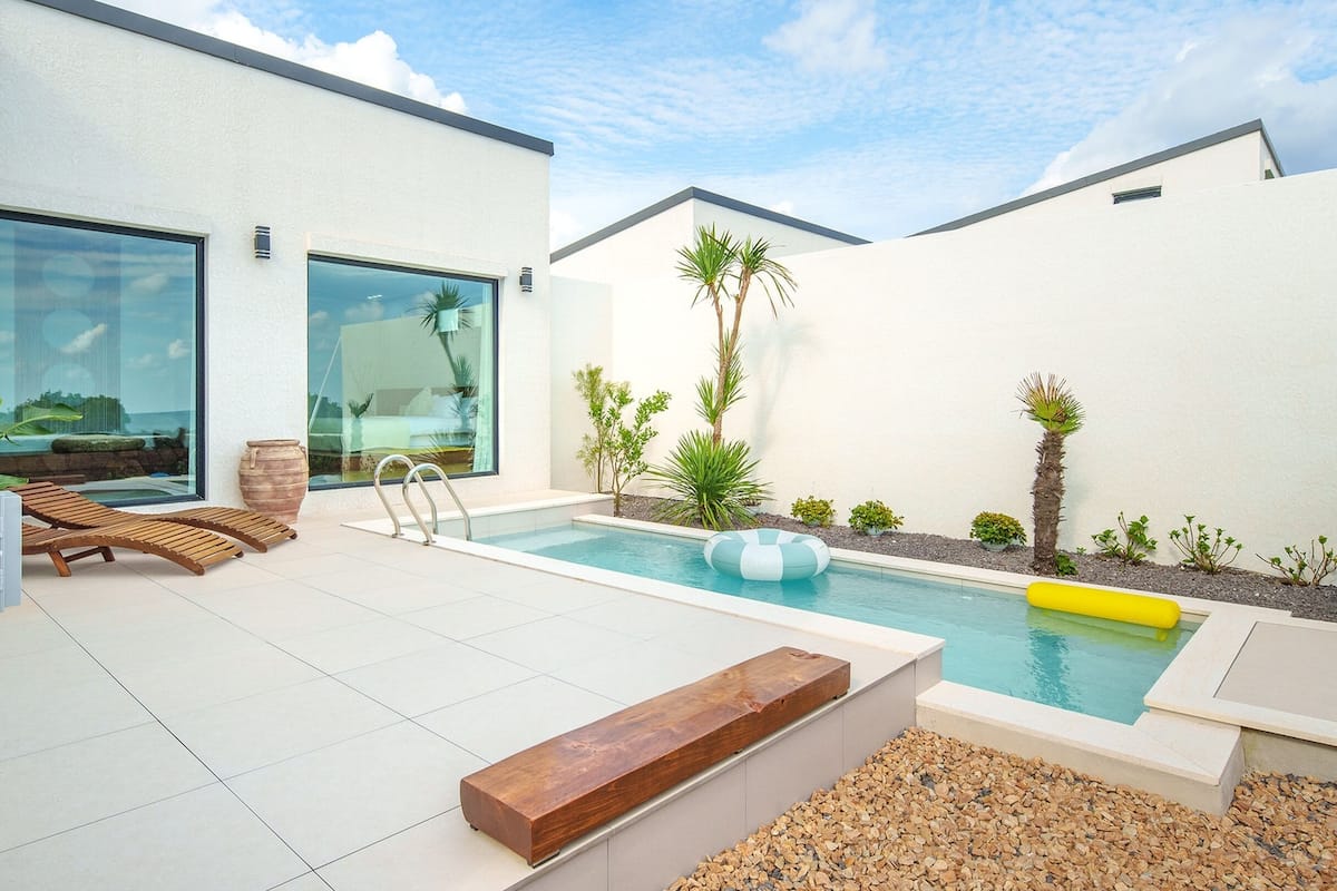 Ein moderner Poolbereich im Freien mit einer Holzterrasse, Liegestühlen und einem kleinen Pool mit einem schwimmenden Ring.