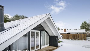 Une maison moderne avec un toit en pente, de grandes portes vitrées et une terrasse en bois.