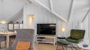 Une chambre de style loft moderne avec un plafond en pente, un grand téléviseur à écran plat, un fauteuil vert et un coin repas comprenant une table et des chaises.