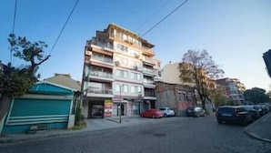 Un immeuble à plusieurs étages, avec un espace commercial au rez-de-chaussée, une devanture visible et un parking avec des voitures.