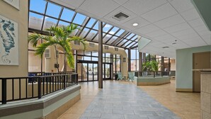 A spacious indoor area with a high ceiling, large windows, and a central seating area with chairs and a small table.