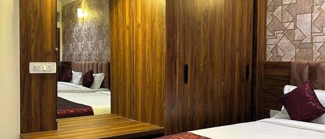 A bedroom with a wooden wardrobe, a bedside table, a bed with a patterned bedspread, and a wall with a geometric design.
