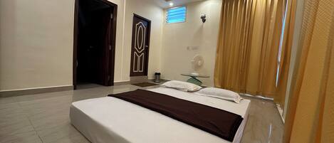 A modern hotel room with a large bed, a ceiling fan, and a window with curtains.