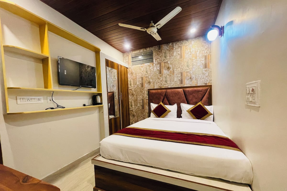Quarto de hotel bem organizado, com uma cama, televisão em uma prateleira e um ventilador de teto.