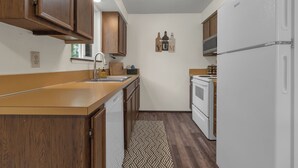 A compact kitchen with wooden cabinets, a white refrigerator, a built-in oven, and a patterned rug. - Quiet 2BR/2BA Olympia townhome on acreage near downtown, Capitol, workspace, garage parking (Olympia)