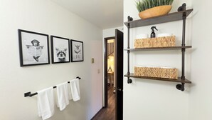 A hallway with a towel rack, framed pictures, and a shelf with baskets. - Quiet 2BR/2BA Olympia townhome on acreage near downtown, Capitol, workspace, garage parking (Olympia)