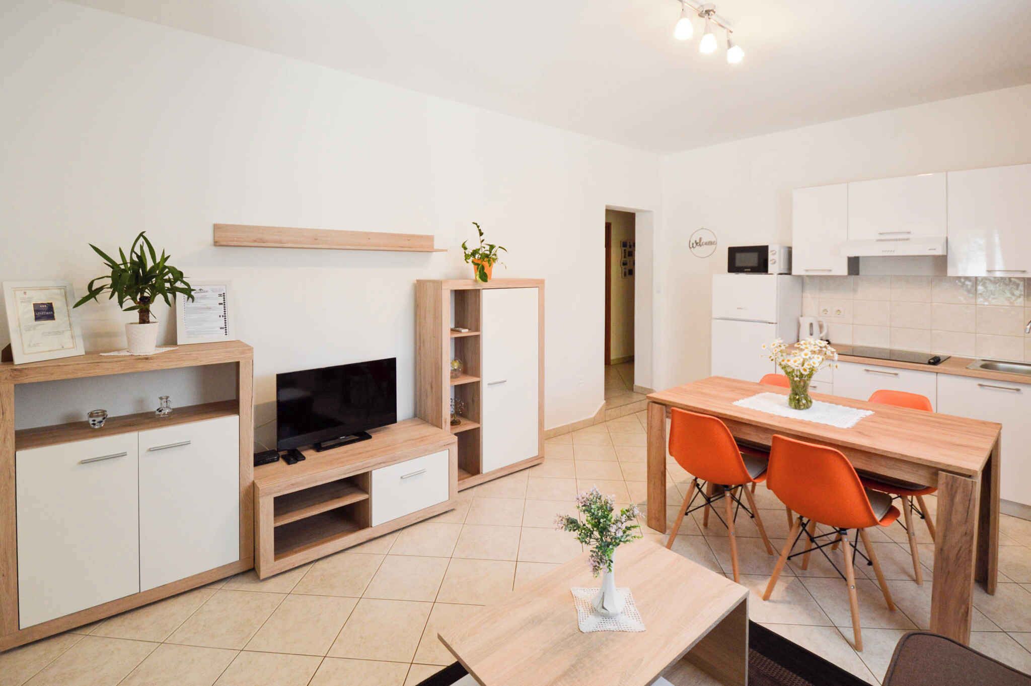 A modern kitchen with white cabinets, a microwave, and a dining area with orange chairs.