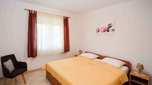 A bedroom with a bed, a chair, a nightstand, a lamp, and a window with curtains. - Apartments in Stinjan/istrien 8432 (Pula)