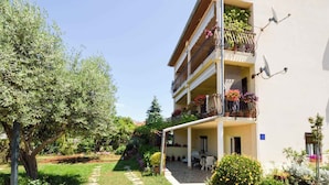 A multi-story building with balconies adorned with flowers, a garden area with a pathway, and a clear blue sky. - Apartments in Stinjan/istrien 8432 (Pula)