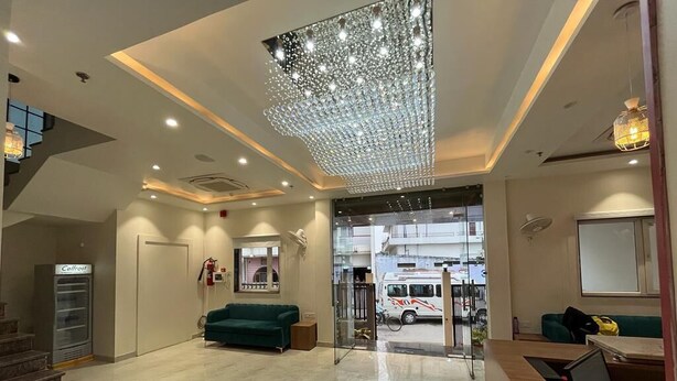 A hotel lobby with a marble floor, a green sofa, a reception desk, and a large chandelier. - Hotel Satsang Grand (Varanasi)