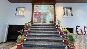 A staircase with potted plants, a wooden ceiling, and a glass door leading to a room with a chandelier. - Hotel Satsang Grand (Varanasi)