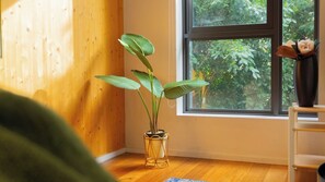 Une pièce dotée d’un plancher en bois, d’une fenêtre donnant sur un paysage verdoyant et d’une plante en pot posée sur un support.