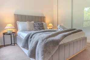 Ein Schlafzimmer mit einem Bett, zwei Nachttischen inklusive Lampen, einer flauschigen, grauen Decke und einem Fenster mit Blick.