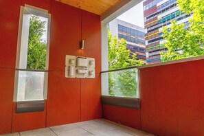 Une pièce avec deux fenêtres, un mur rouge et une vue sur un immeuble moderne.