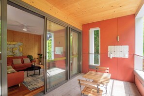 Un intérieur moderne avec un mur rouge, un plafond en bois, une porte coulissante en verre donnant sur un balcon, un canapé rouge, une petite table et un banc en bois.
