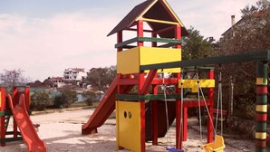 Un parque infantil con una estructura de escalada amarilla y roja, un tobogán rojo y columpios.