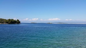 A calm sea with clear waters, a distant island, and a coastline with trees.