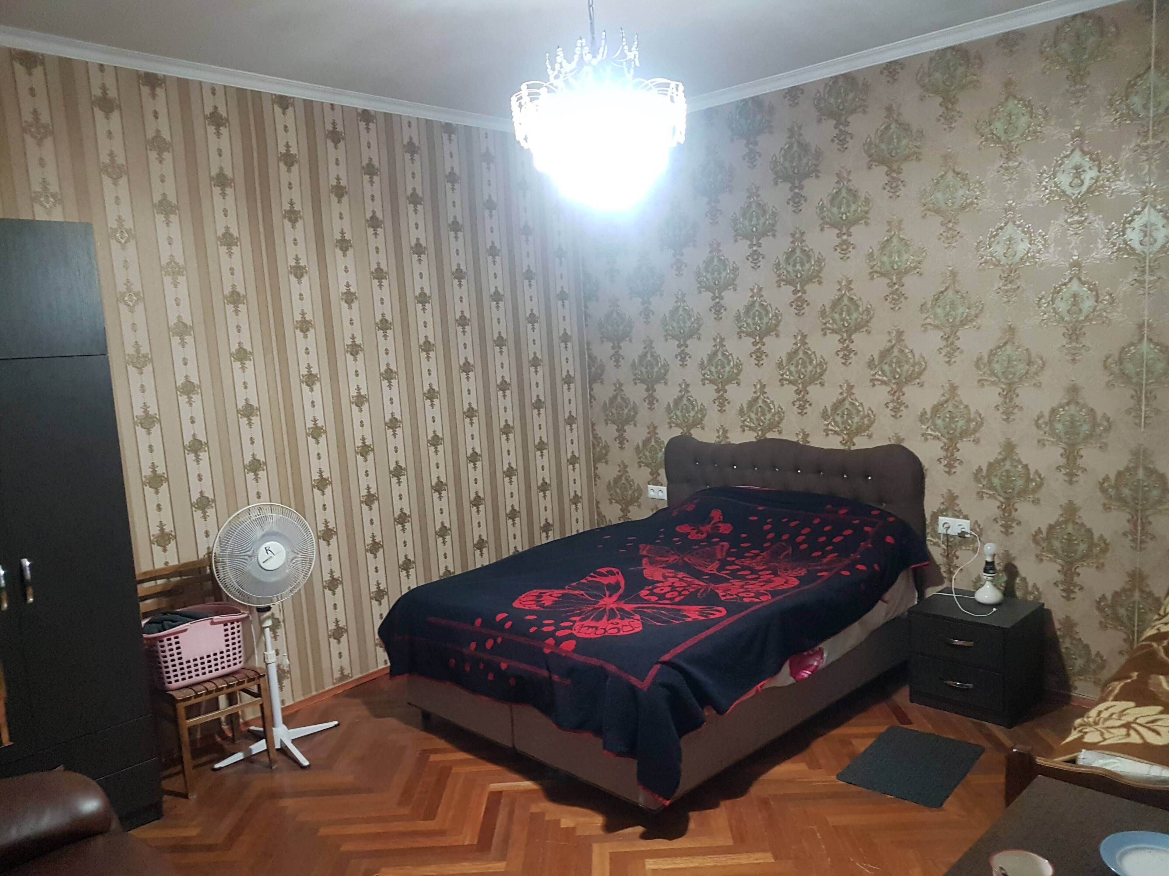 A bedroom with a bed, a standing fan, a dresser, and a chandelier.