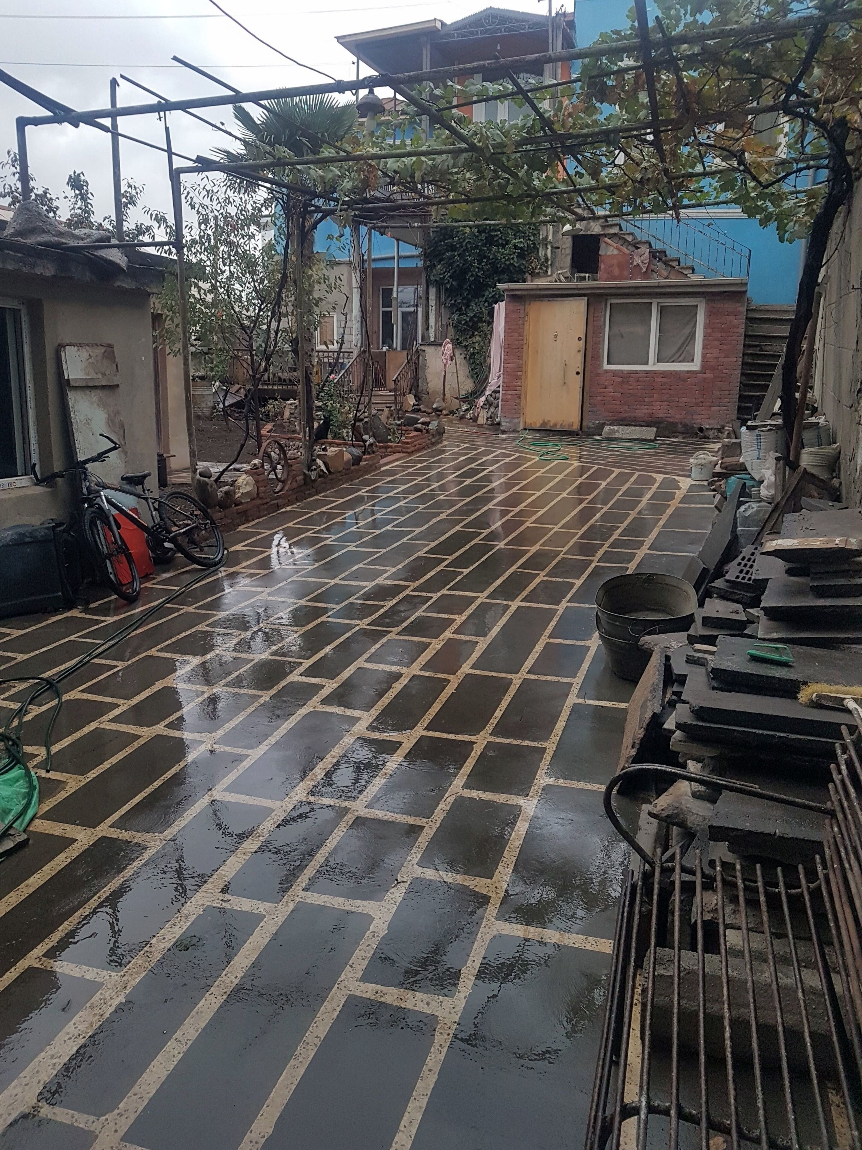 Un patio con suelo de baldosas, una bicicleta y diversos materiales de construcción.