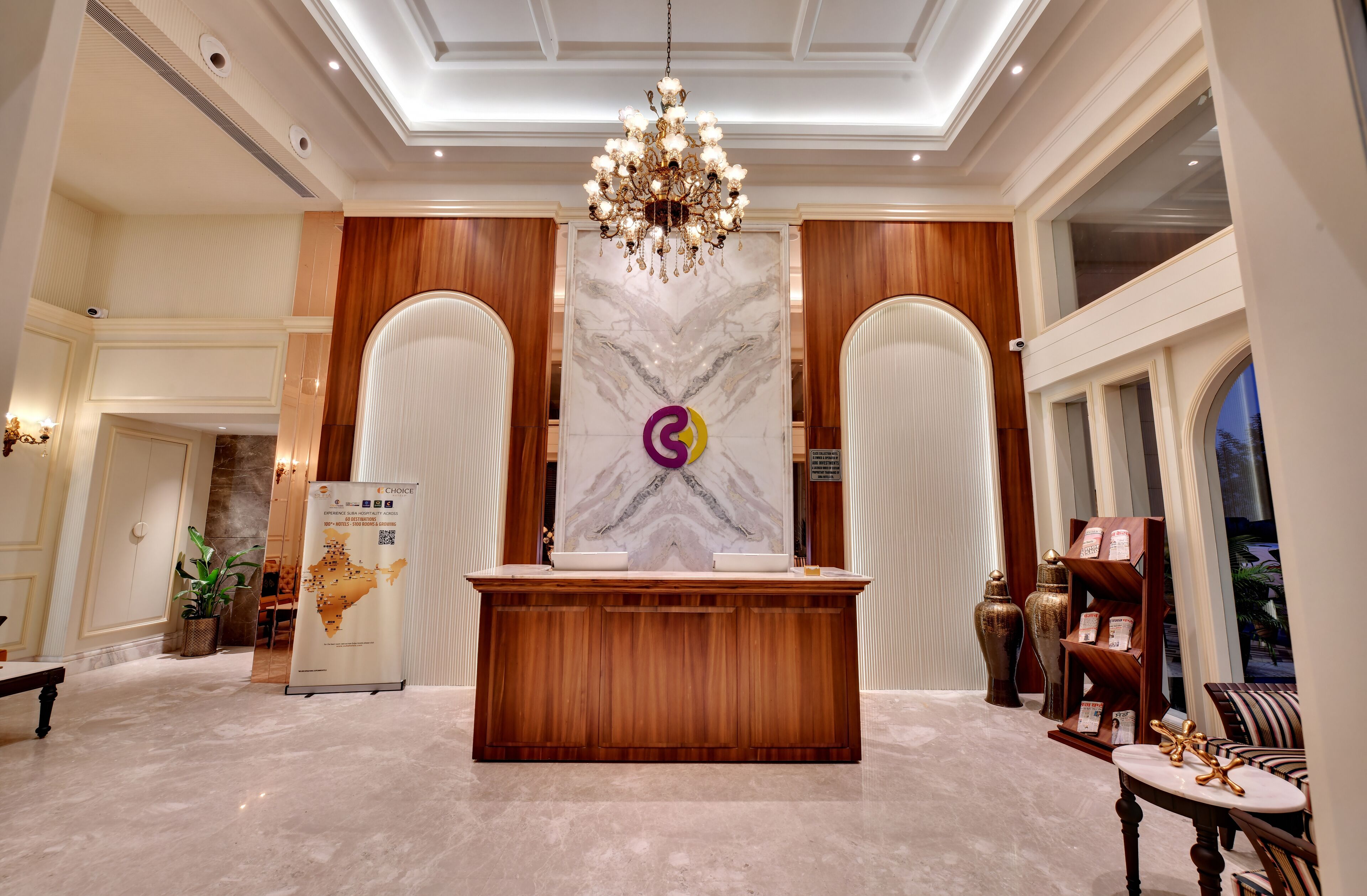 A reception area with a wooden reception desk, a marble wall with a logo, a chandelier, and a view of the outside through a window.