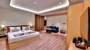A modern hotel room with a large bed, a sofa, a TV, and a desk with a basket of snacks. - Click Collection Amritsar (Amritsar)