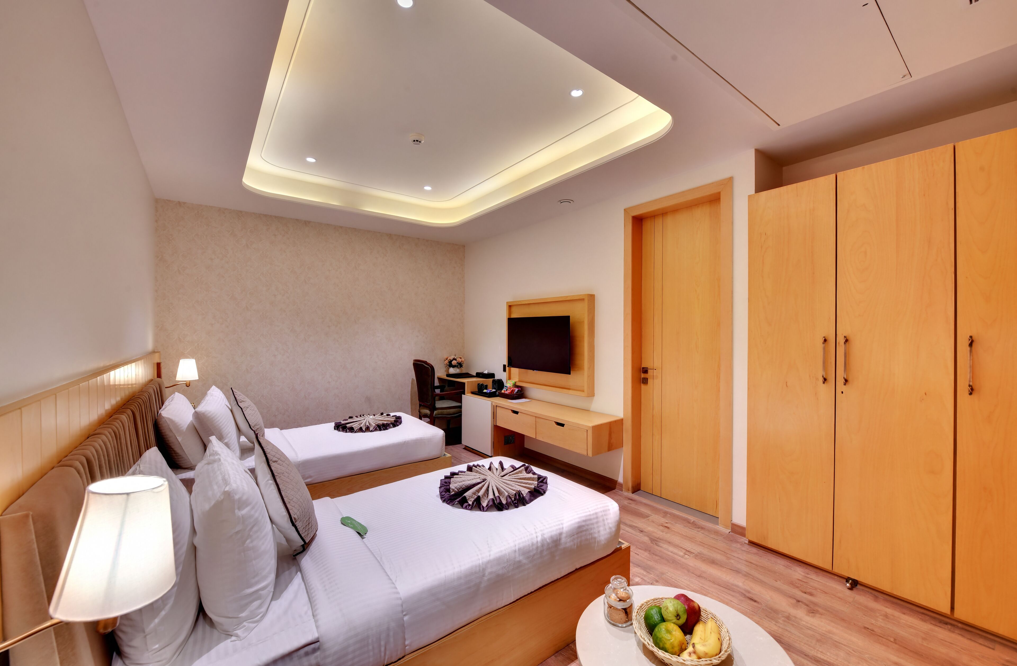 Een hotelkamer met twee bedden, een televisie, een kledingkast en een klein tafeltje met fruit.