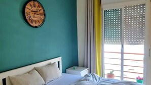 A bedroom with a bed, a wall clock, a nightstand, a window with curtains, and a hanging light fixture. - Charming condo in pleasant Rabat with WiFi (Temara)