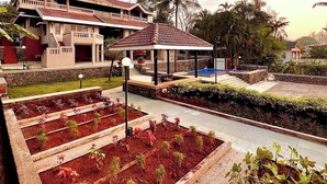 A two-story building with a covered patio area, a swimming pool, and a garden with raised beds.