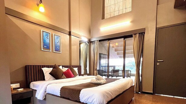 A modern hotel room with a large bed, a nightstand, a seating area with a view, and a door.