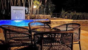 An outdoor pool area with a water feature, surrounded by wicker chairs and palm trees.