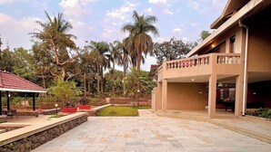 A spacious outdoor area with a stone-paved courtyard, a covered seating area, and a building with a balcony.