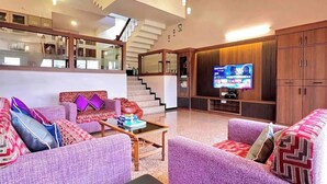 A spacious living area with a sofa set, a coffee table, and a flat-screen TV mounted on the wall.