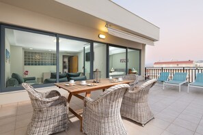 A balcony with wicker furniture, a table set with cups and plates, and a view of the interior through large glass doors. - Side Sea View apartment (Chania)