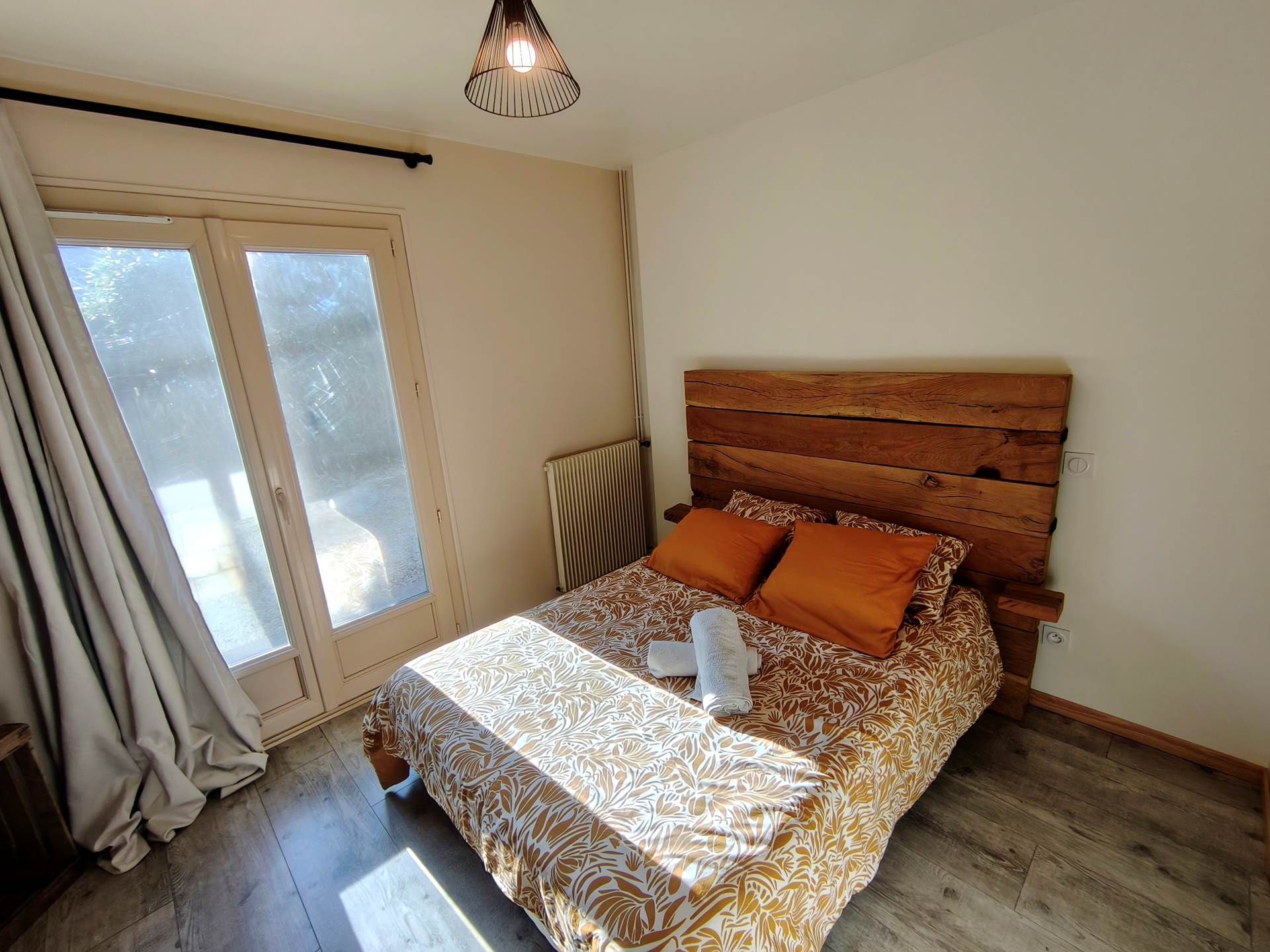 Un dormitorio con cabecera de madera, colcha estampada y un par de toallas sobre la cama.