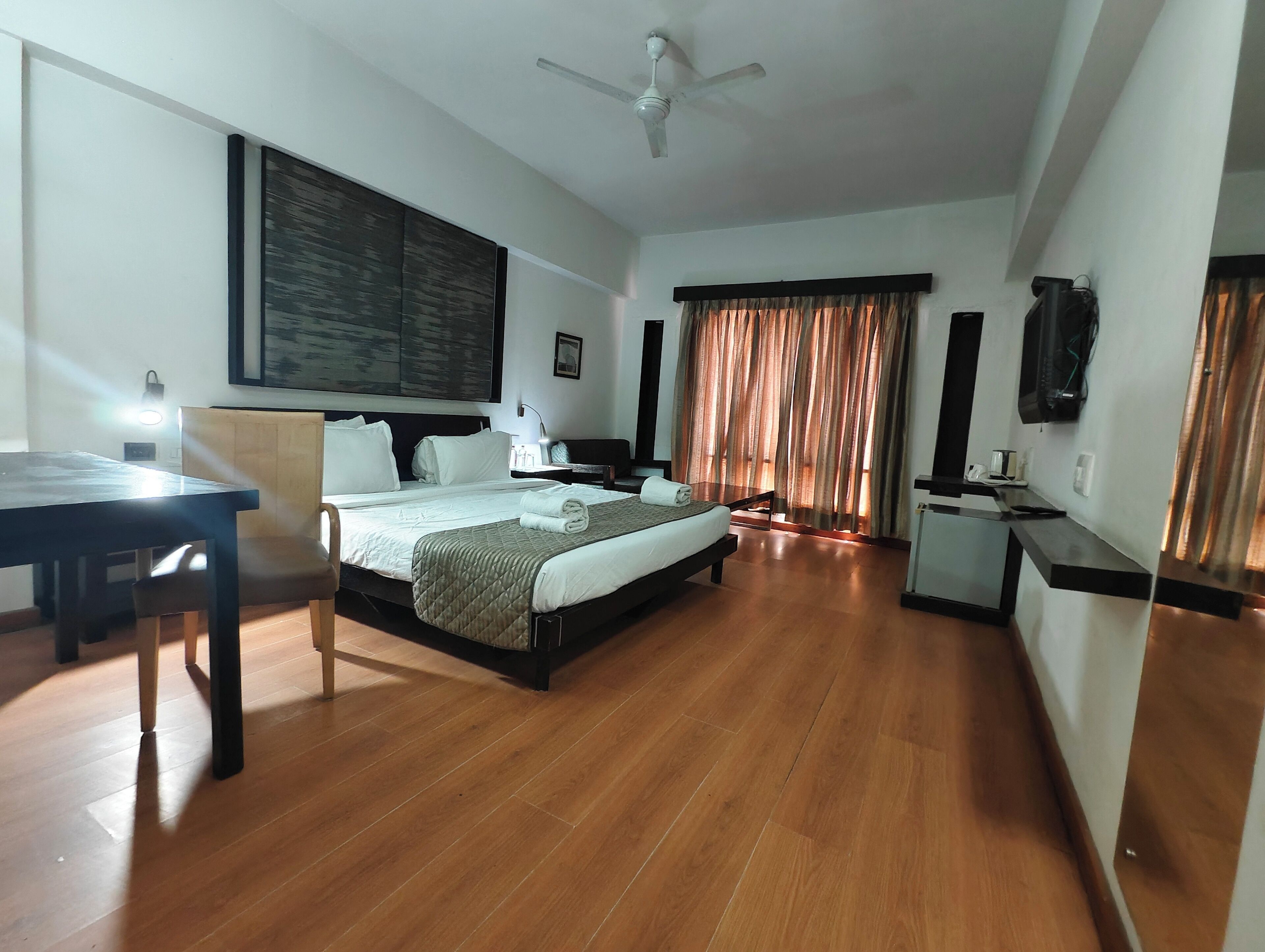 A hotel room with a bed, desk, chair, bedside table, and a ceiling fan.