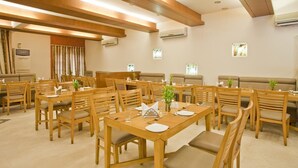 Un comedor con mesas y sillas de madera, unidades de aire acondicionado en las paredes, y una zona de estar con bancos acolchados.