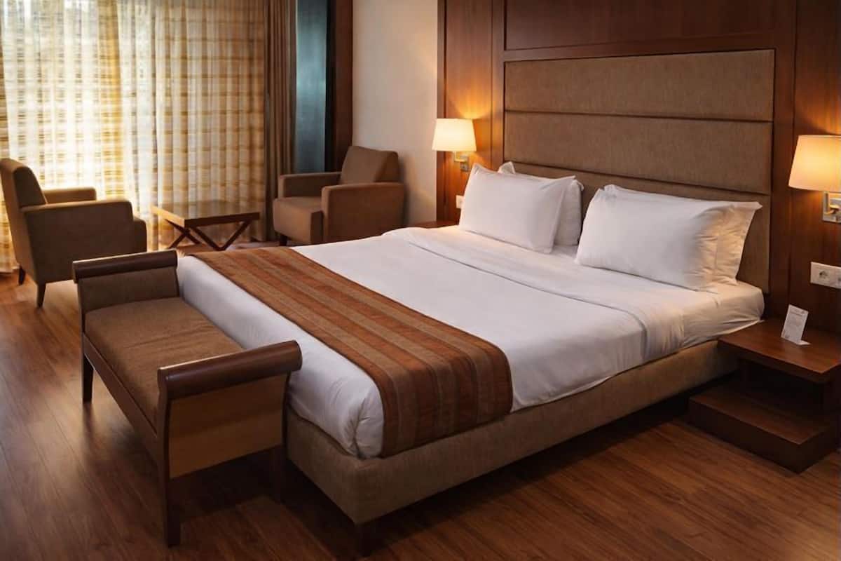 Hotellihuone, jossa on suuri sänky, kaksi yöpöytää valaisimineen, sohva ja nojatuoli.