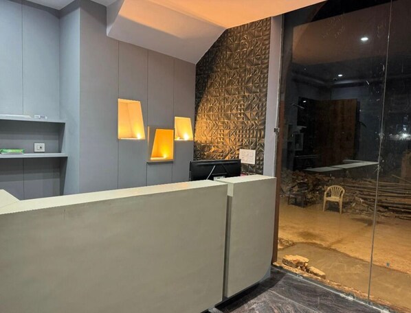 Un espace d’accueil au design moderne, comprenant un comptoir de réception, deux lampes fixées au mur et un mur décoratif en pierre.