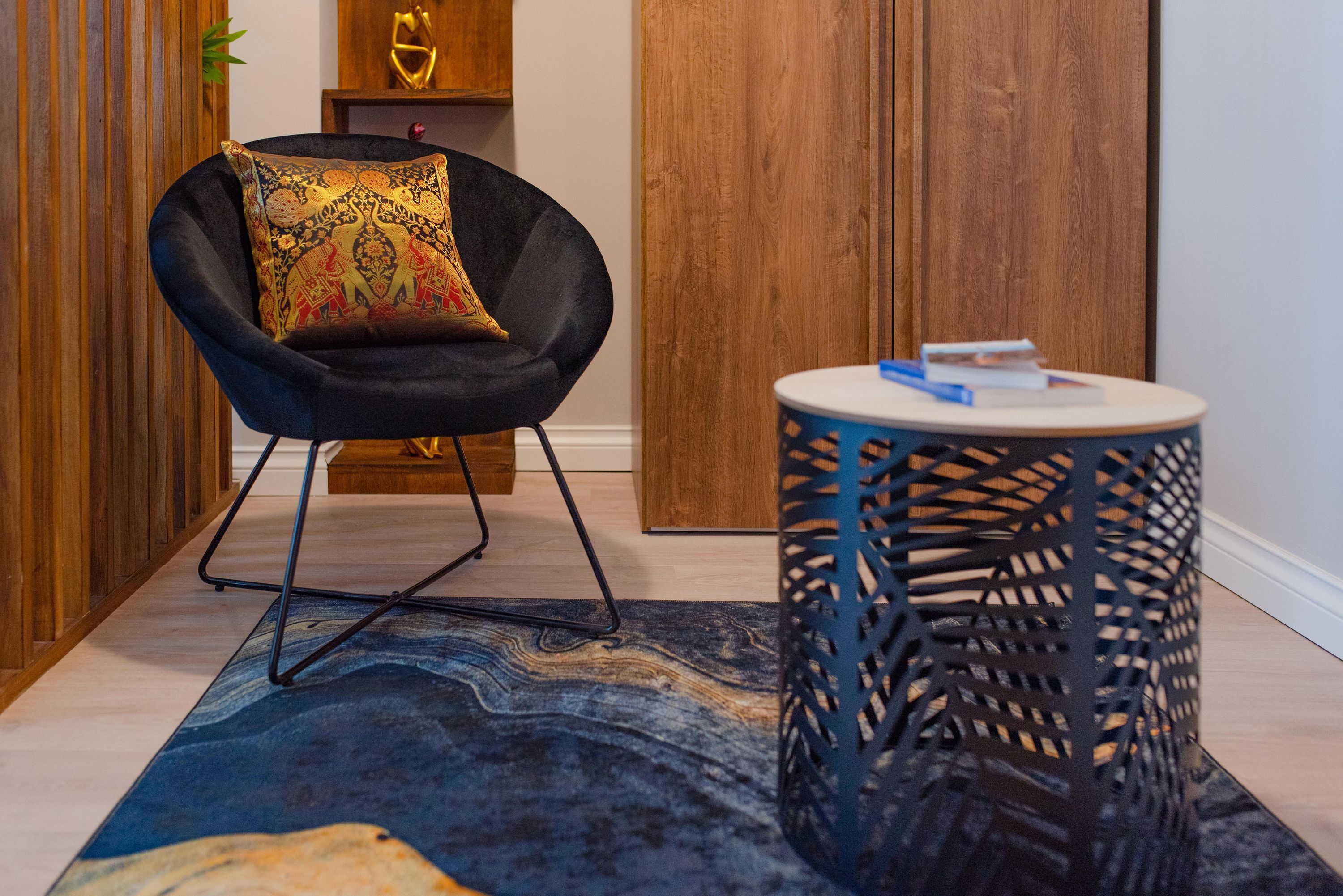 A modern room with a black chair, a round side table, a patterned rug, and wooden paneling.