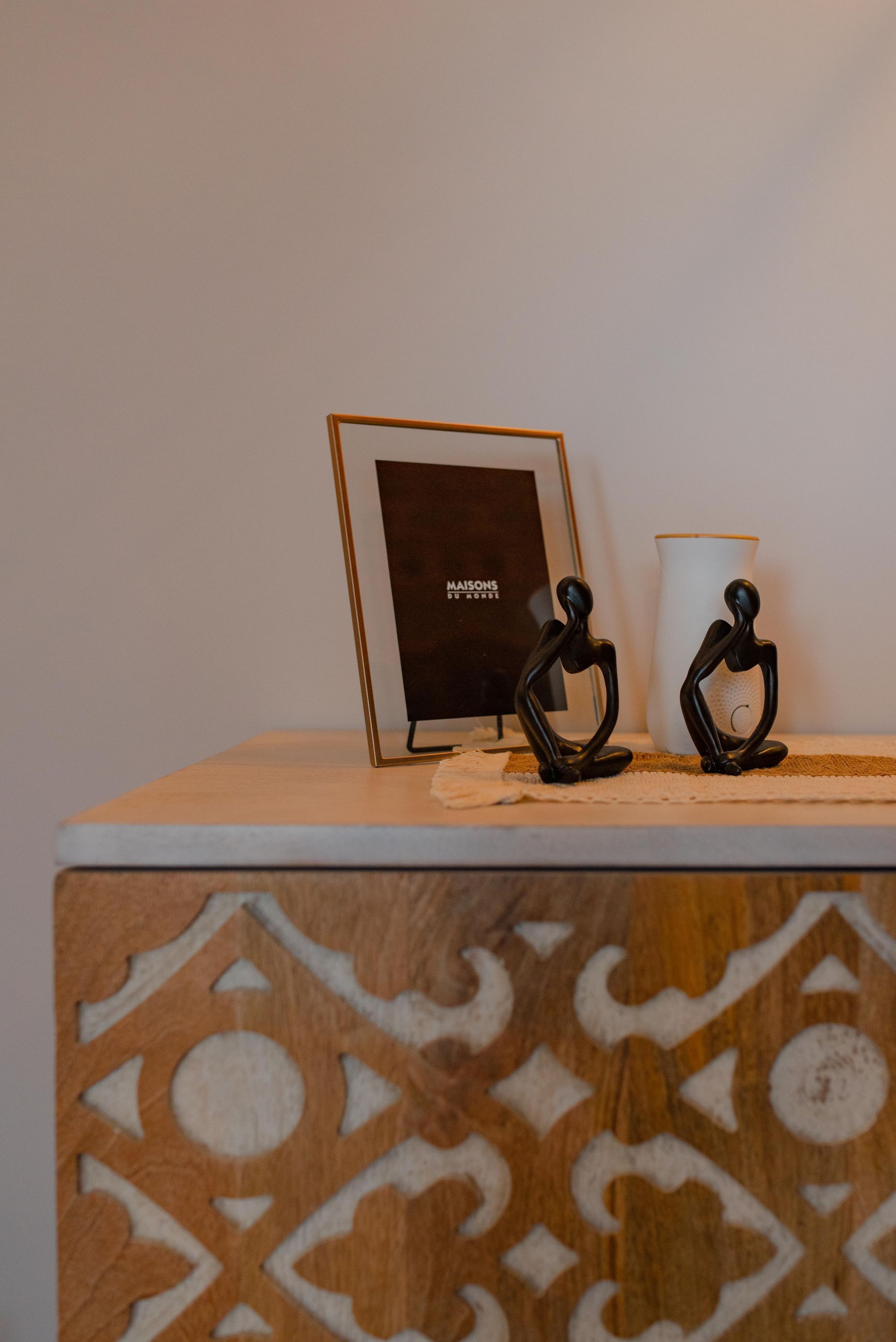 A small table with a framed picture, two black sculptures, and a white vase.