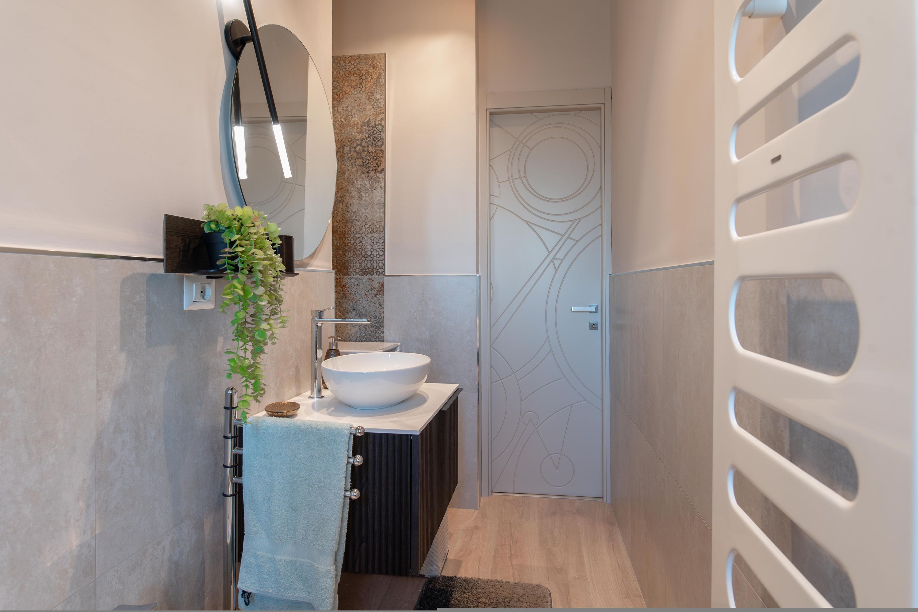 Un bagno moderno con uno specchio rotondo, un lavandino bianco e un portascopevoli.