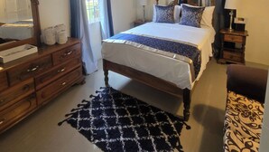 A bedroom with a wooden bed, a ceiling fan, a dresser, and a patterned rug.