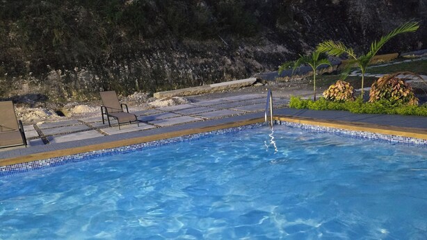 A clear blue pool with a tiled edge, surrounded by lounge chairs and a rocky landscape in the background.