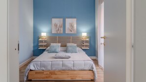 Un dormitorio con cama de madera, paredes azules y dos lámparas fijadas a la pared.