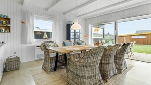 A dining area with a wooden table and wicker chairs, white paneled walls, and large windows. - Gorgeous home in Ebeltoft with sauna (Ebeltoft)
