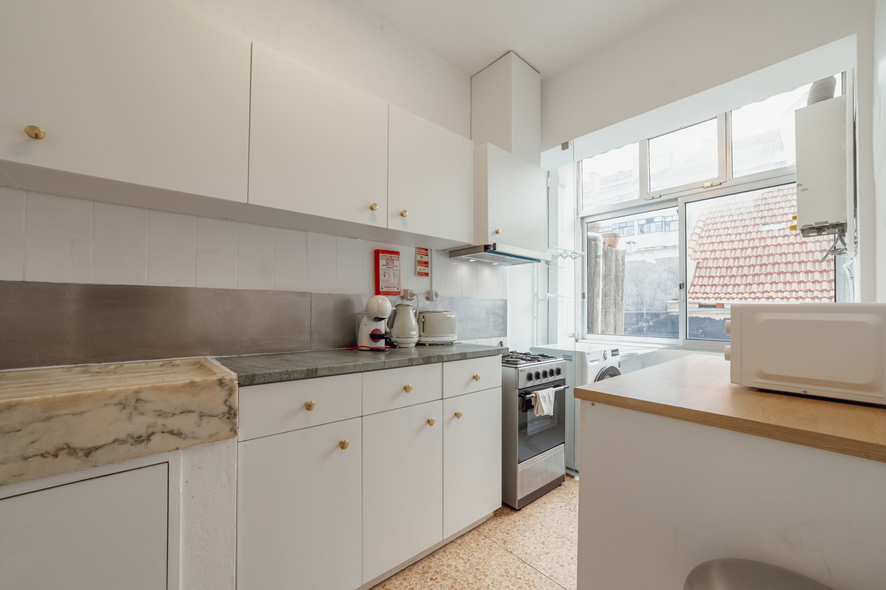 A modern kitchen with white cabinets, a marble countertop, a stove, and a window with a view of a building.