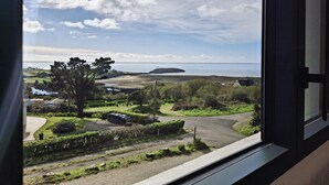 A view from a window overlooking a coastal landscape with a road, greenery, and a distant island. - Elegance on the bay, modern apartment with garden and sea view (Crozon)