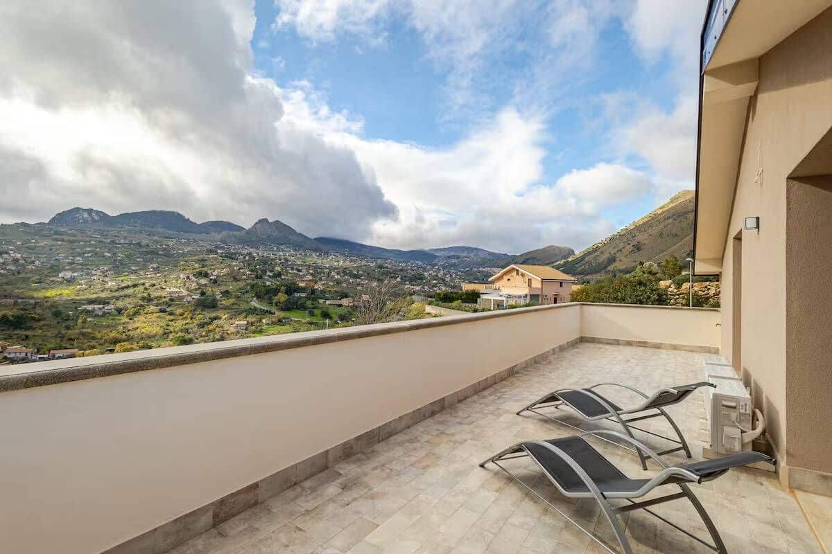 A balcony with a view of a mountainous landscape, a chair, and a small table.