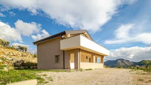 A modern single-story house with a flat roof, large windows, and a stone wall to the left. -  Home Sweet Home (Monreale)