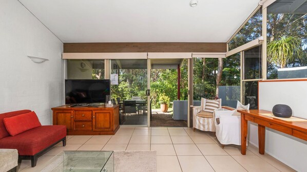 A modern living room with a TV, red sofa, wooden cabinet, and a dining area with a table and chairs.